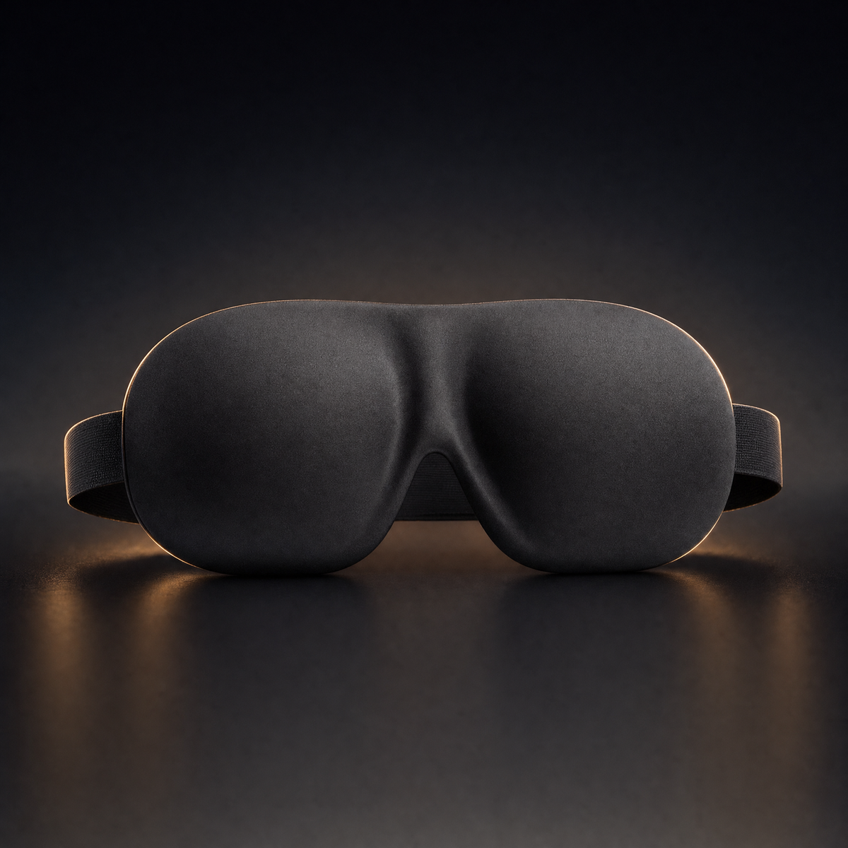 Matte black contoured 3D sleep mask on a dark background with warm rim lighting